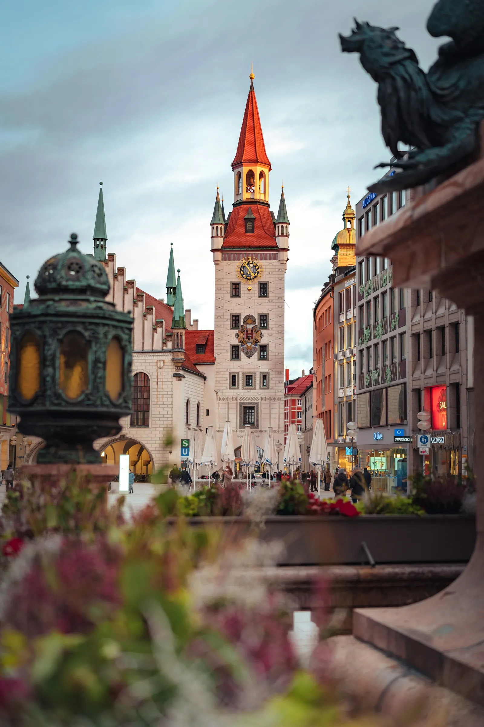 Altes Rathaus am Marienplatz in München mit rotem Turmhelm, davor eine Bronzefigur und Blumen
