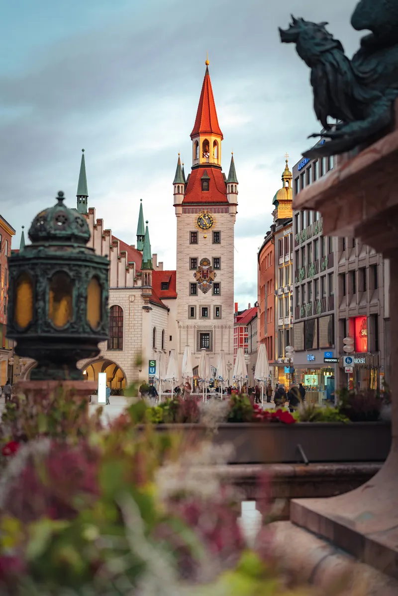 Altes Rathaus am Marienplatz in München mit rotem Turmhelm, davor eine Bronzefigur und Blumen